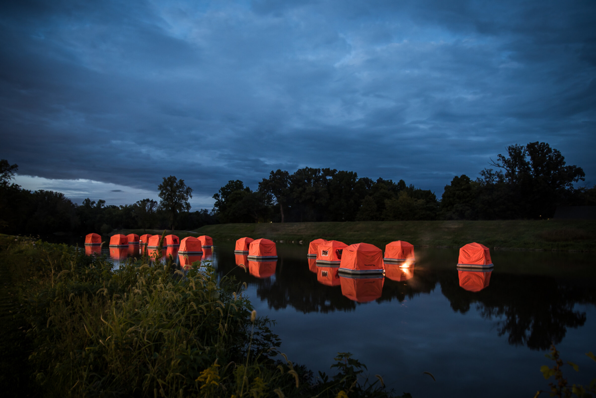 A row of illuminated SmithFly Shoal Tents floating on a lake at dusk